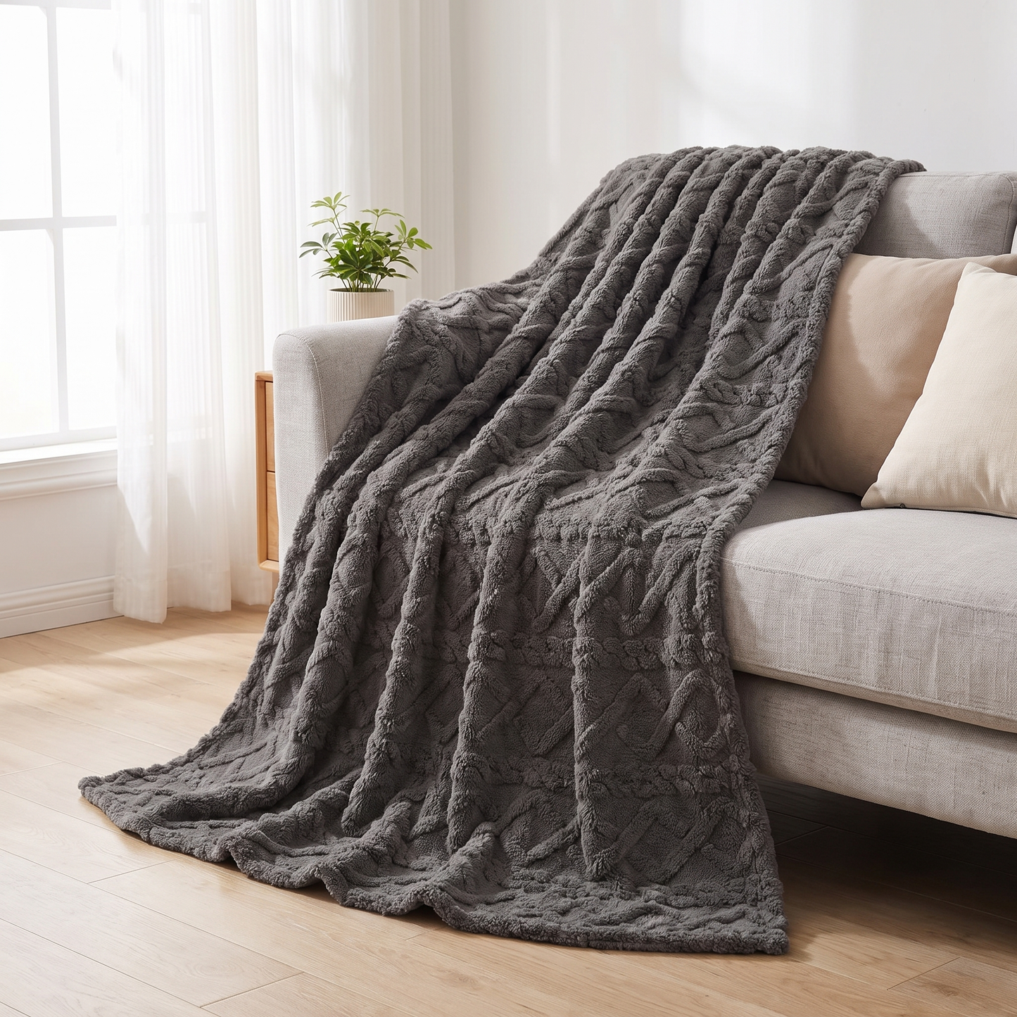 Kuscheldecke mit Zopfmuster in Dunkelgrau über einem Sofa im hellen Wohnzimmer