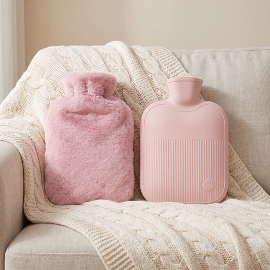 Wärmflasche und weicher Stoffbezug in Pink nebeneinander auf einer Kuscheldecke